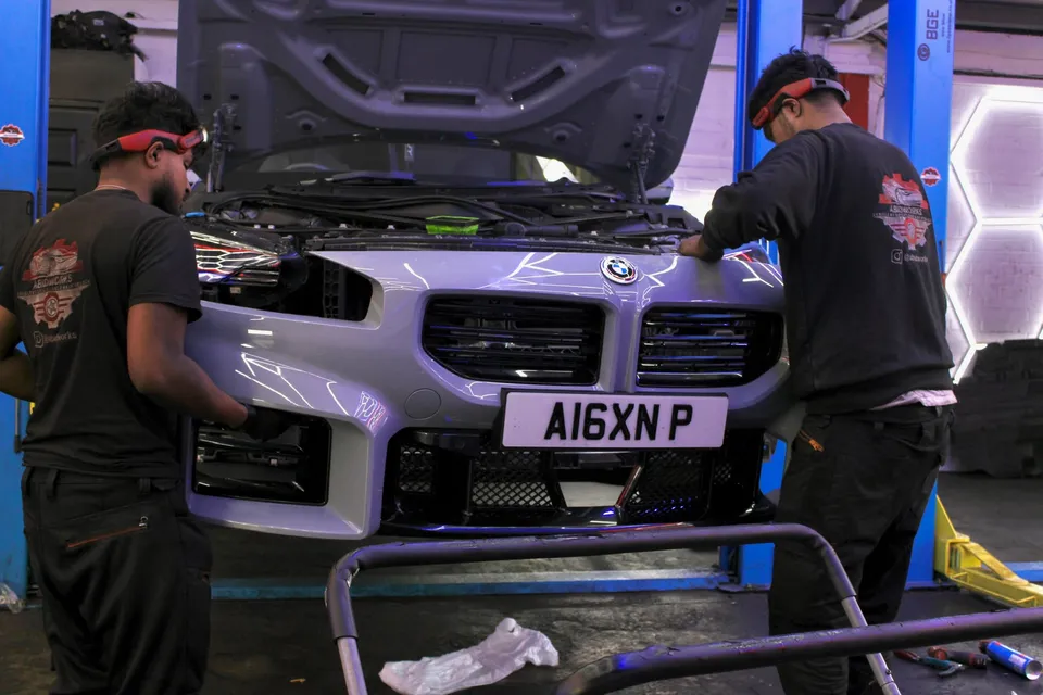 Two technicians working on the front of a BMW M2 in the workshop