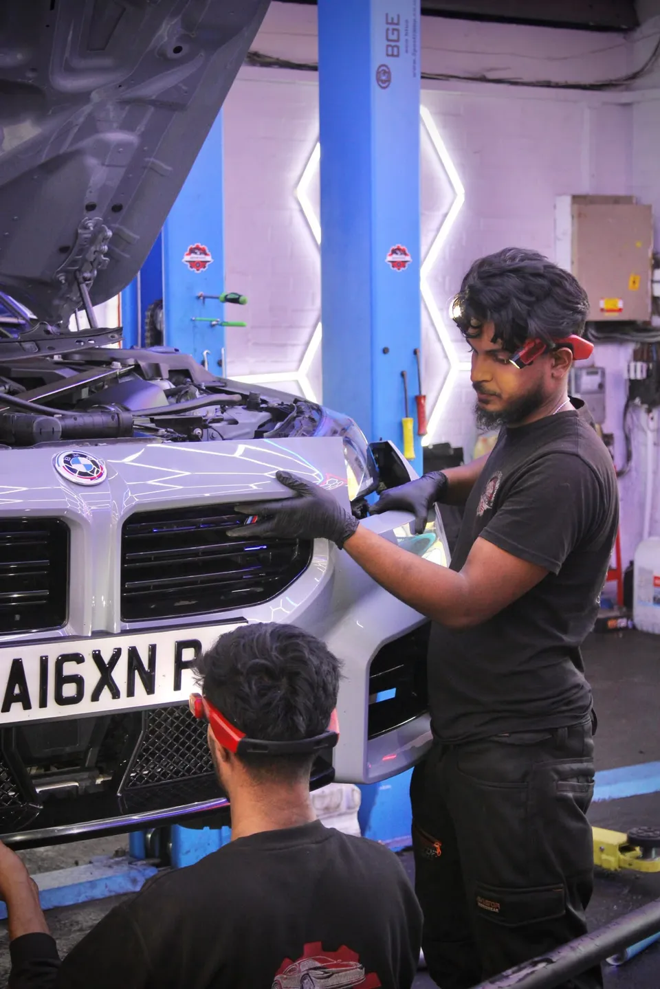 Two technicians working on the front of a BMW M2