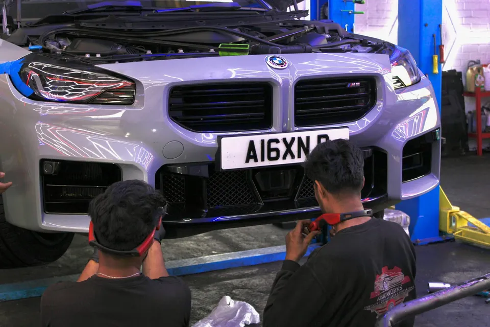 Two technicians working on the front bumper of a BMW M2